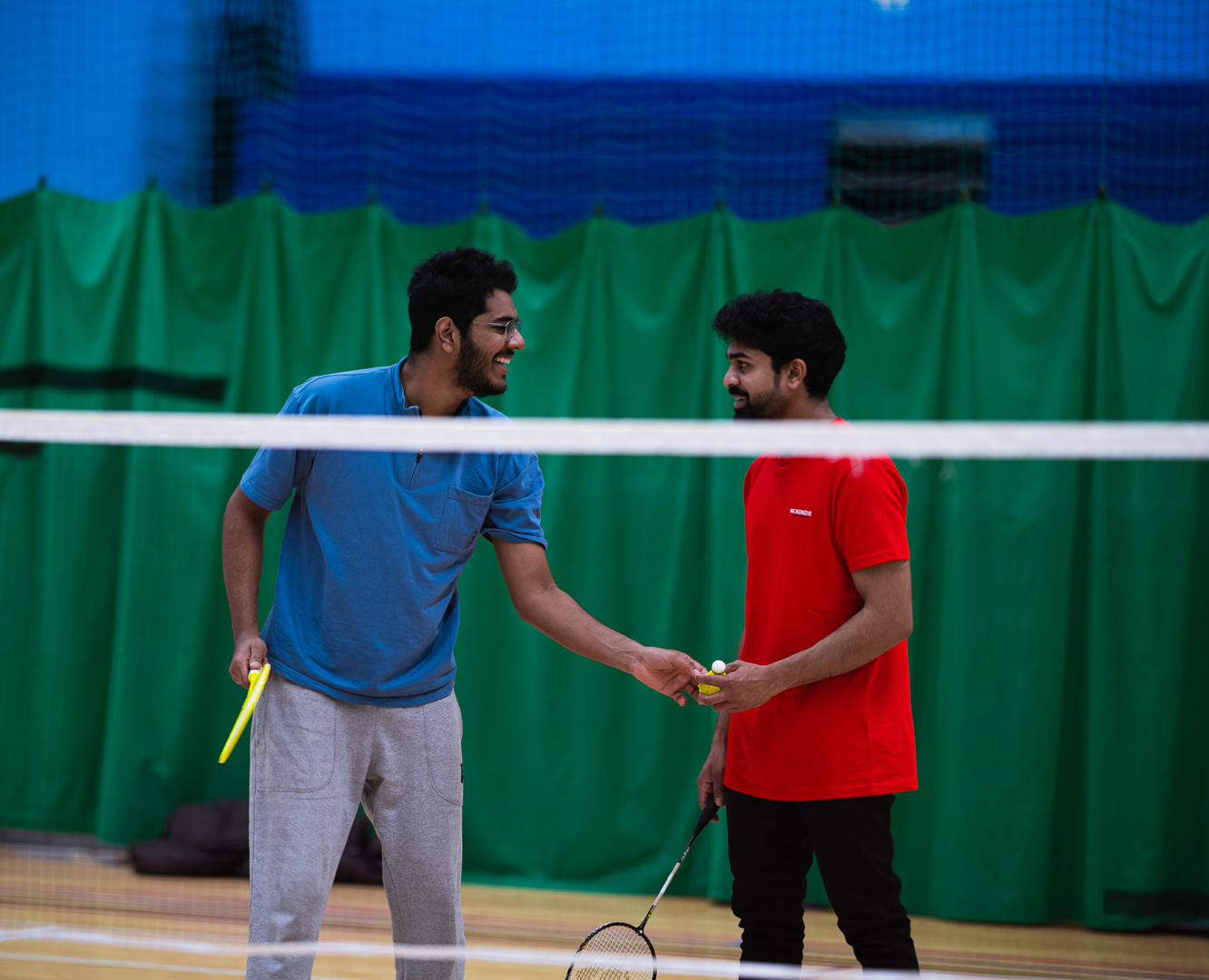Two men on a badminton court exchanging a shuttlecock, each holding a racket.