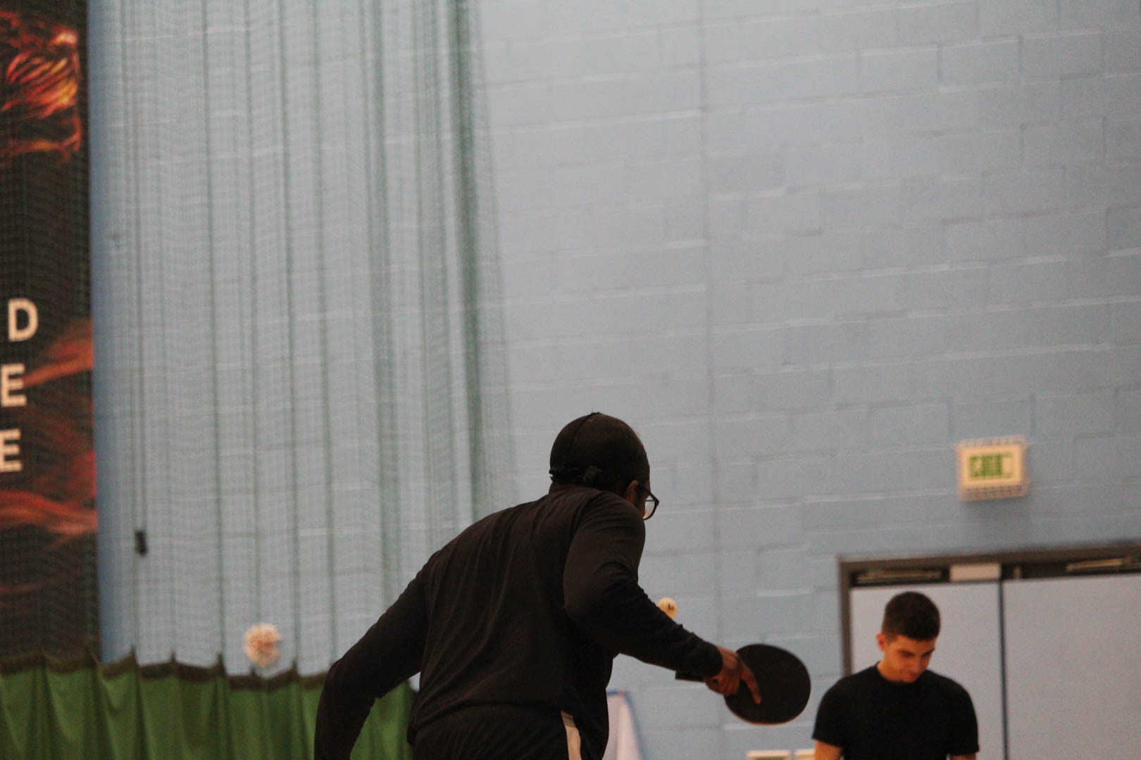 Two people playing table tennis indoors. 