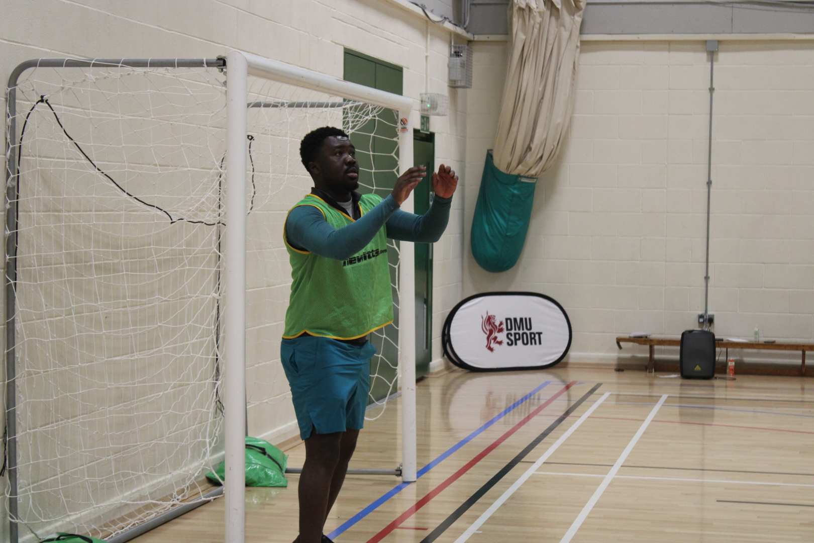 Goalkeeper in bib prepares to make save in an indoor sports hall.