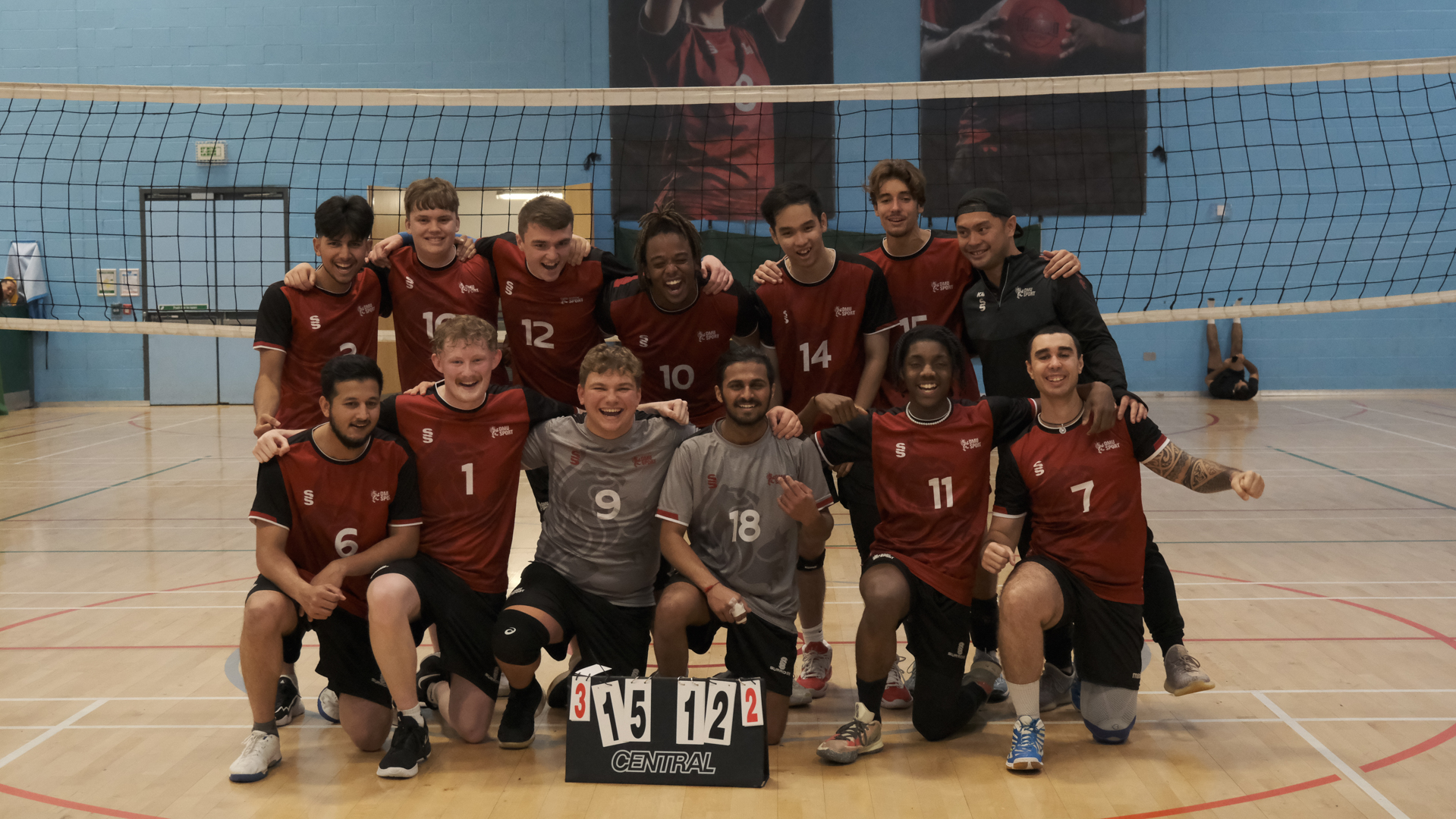 Volleyball team posing together on an indoor court, wearing matching red and black uniforms.