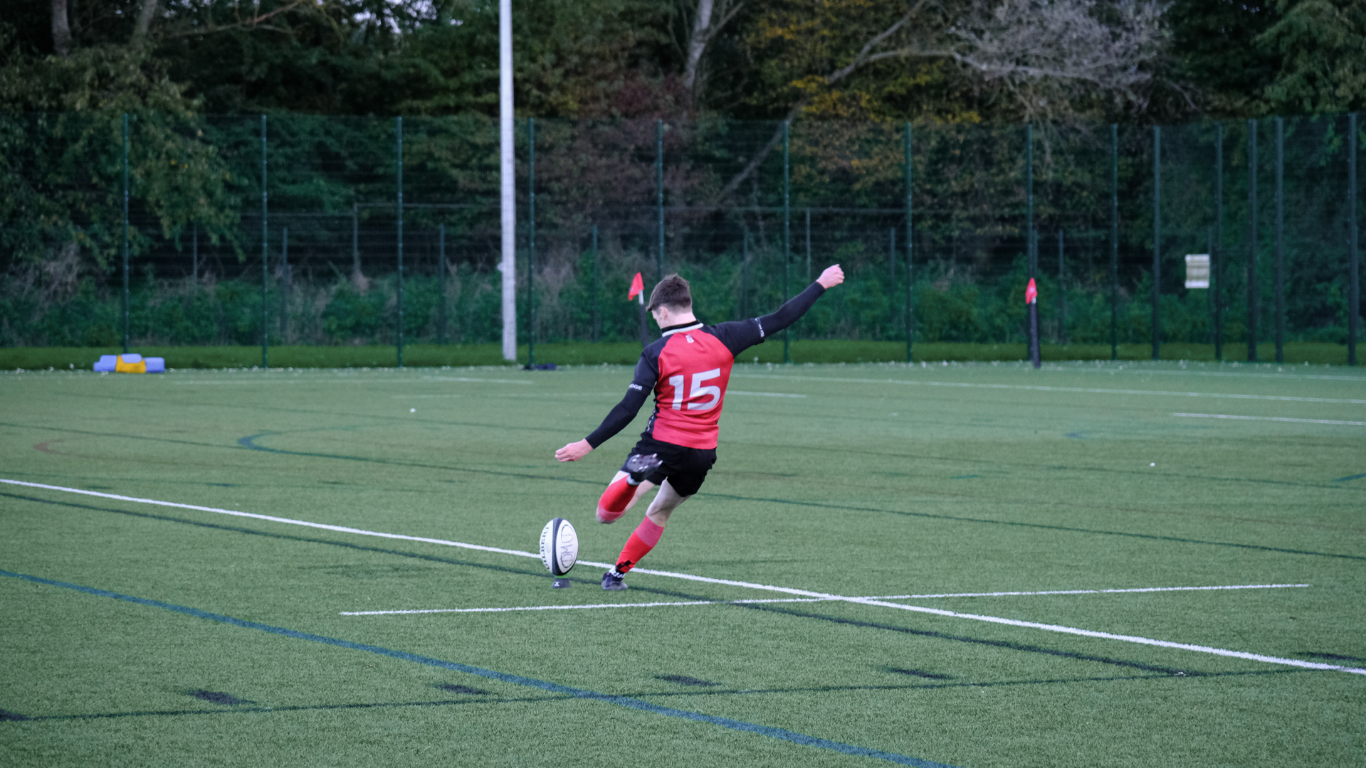 Rugby player in a red jersey kicking a ball on a green field.