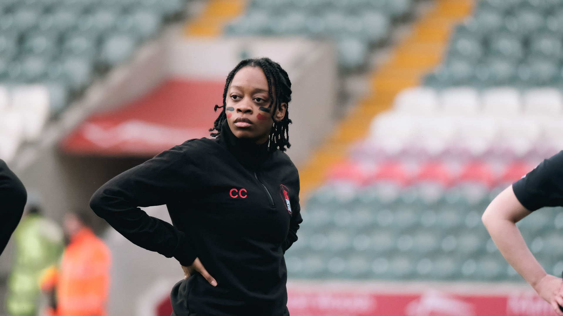 Person wearing a black hoodie standing in a stadium with empty seats in the background.