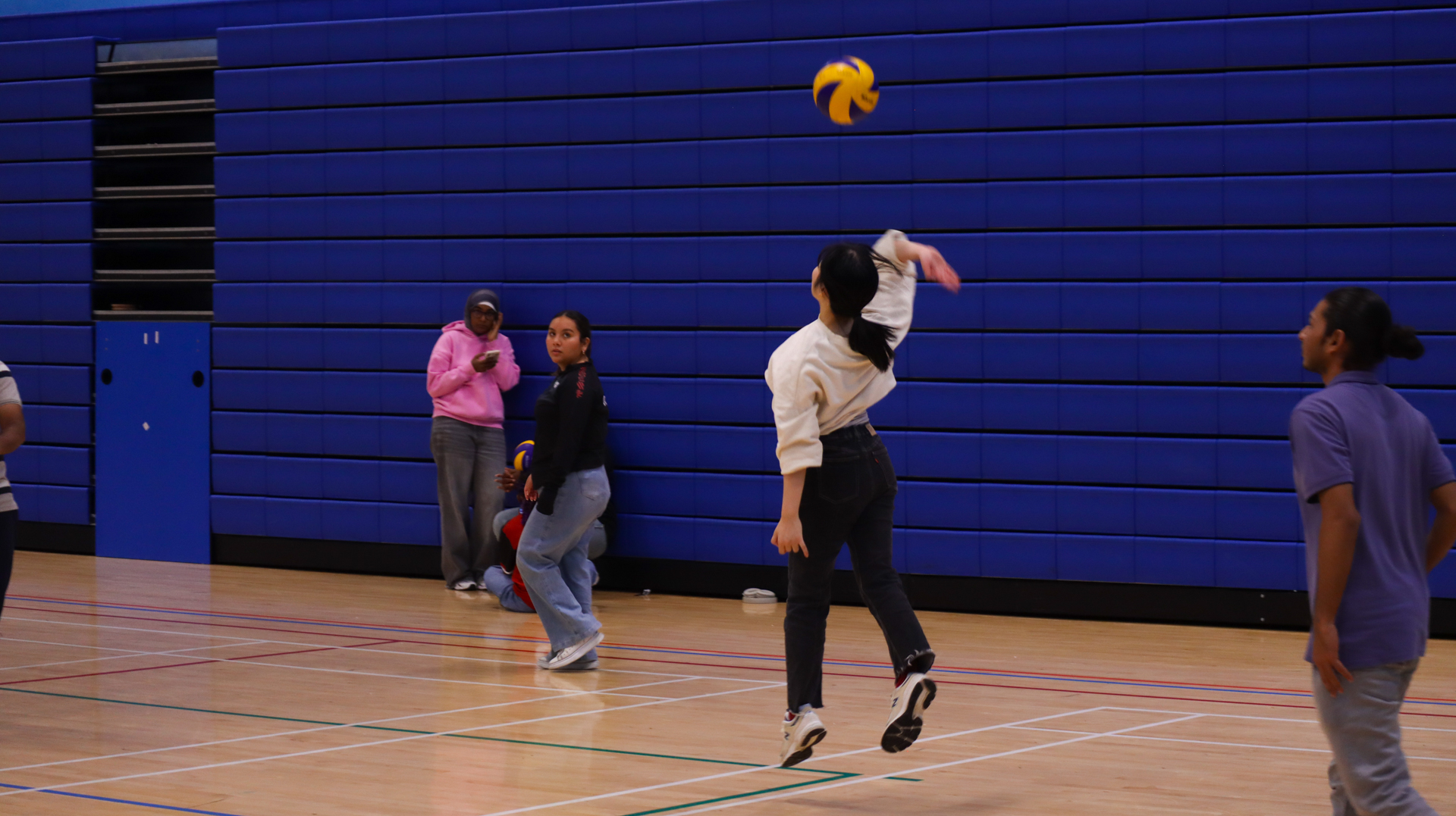 A group of people playing volleyball indoors, with one person jumping to hit the ball.