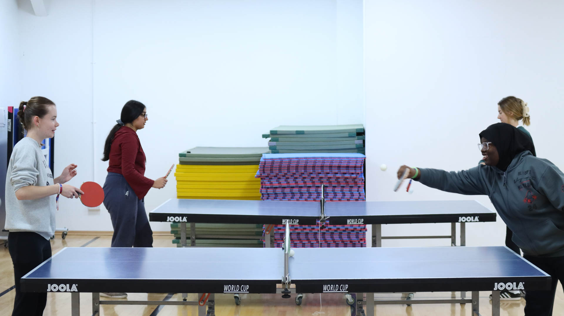 Four people playing table tennis indoors.