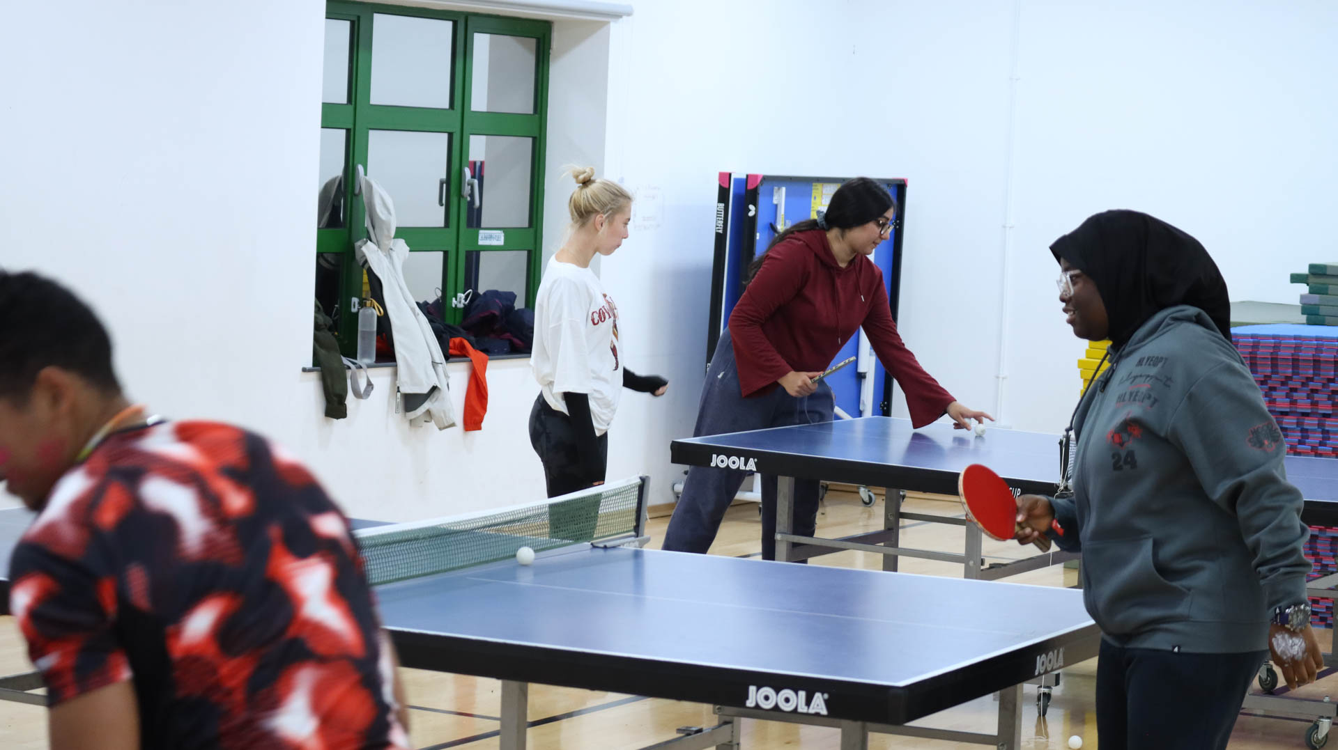 Four people playing table tennis in a brightly lit indoor room.