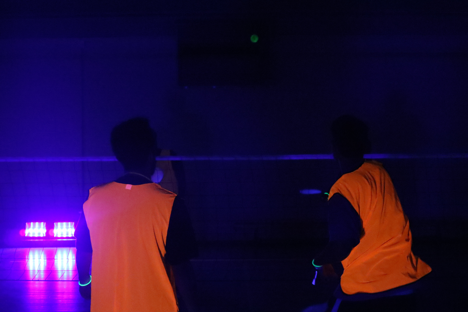 People playing badminton in a dark setting illuminated by a neon light.