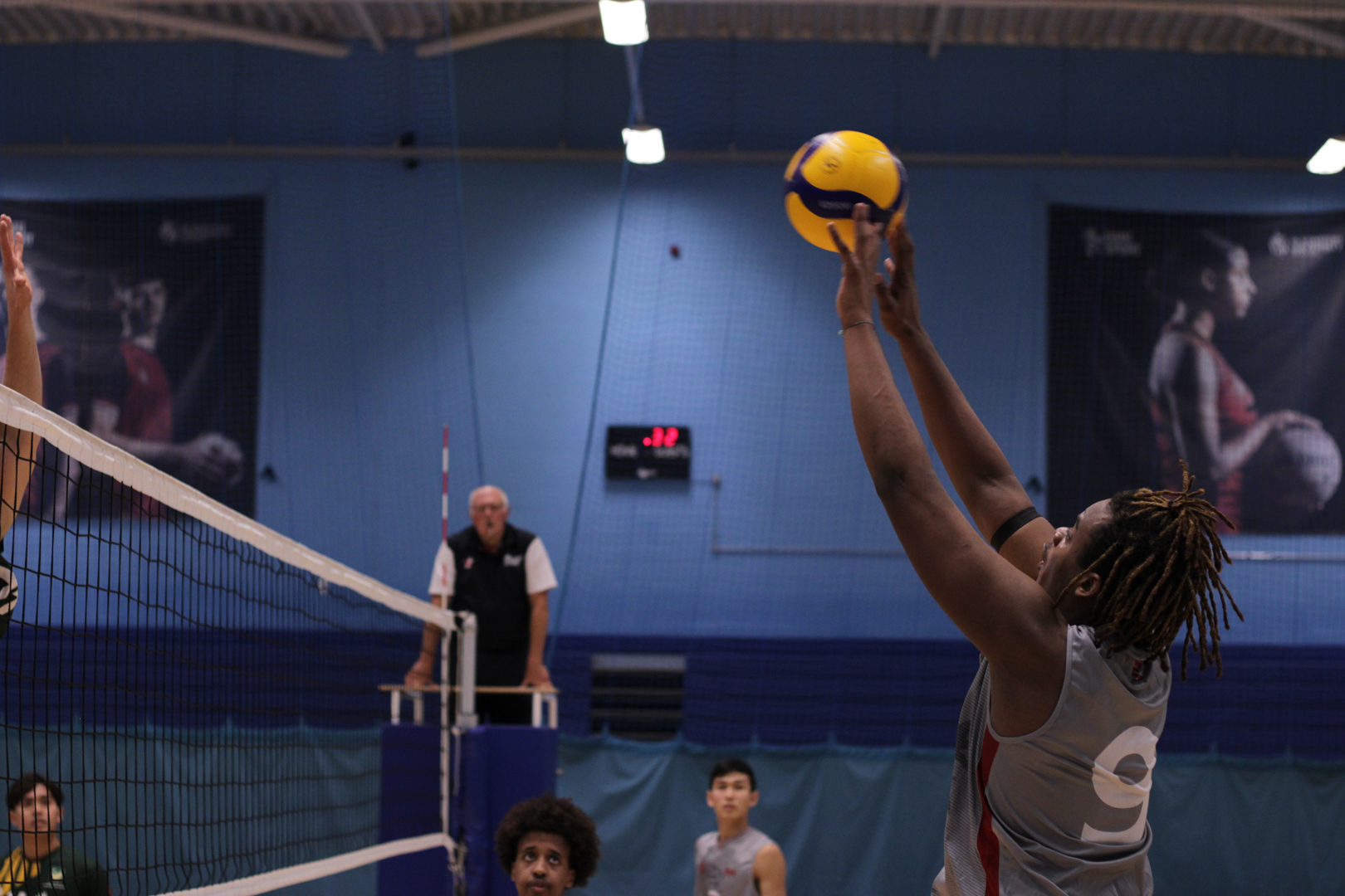 Volleyball player jumping to hit the ball over the net during an indoor match.