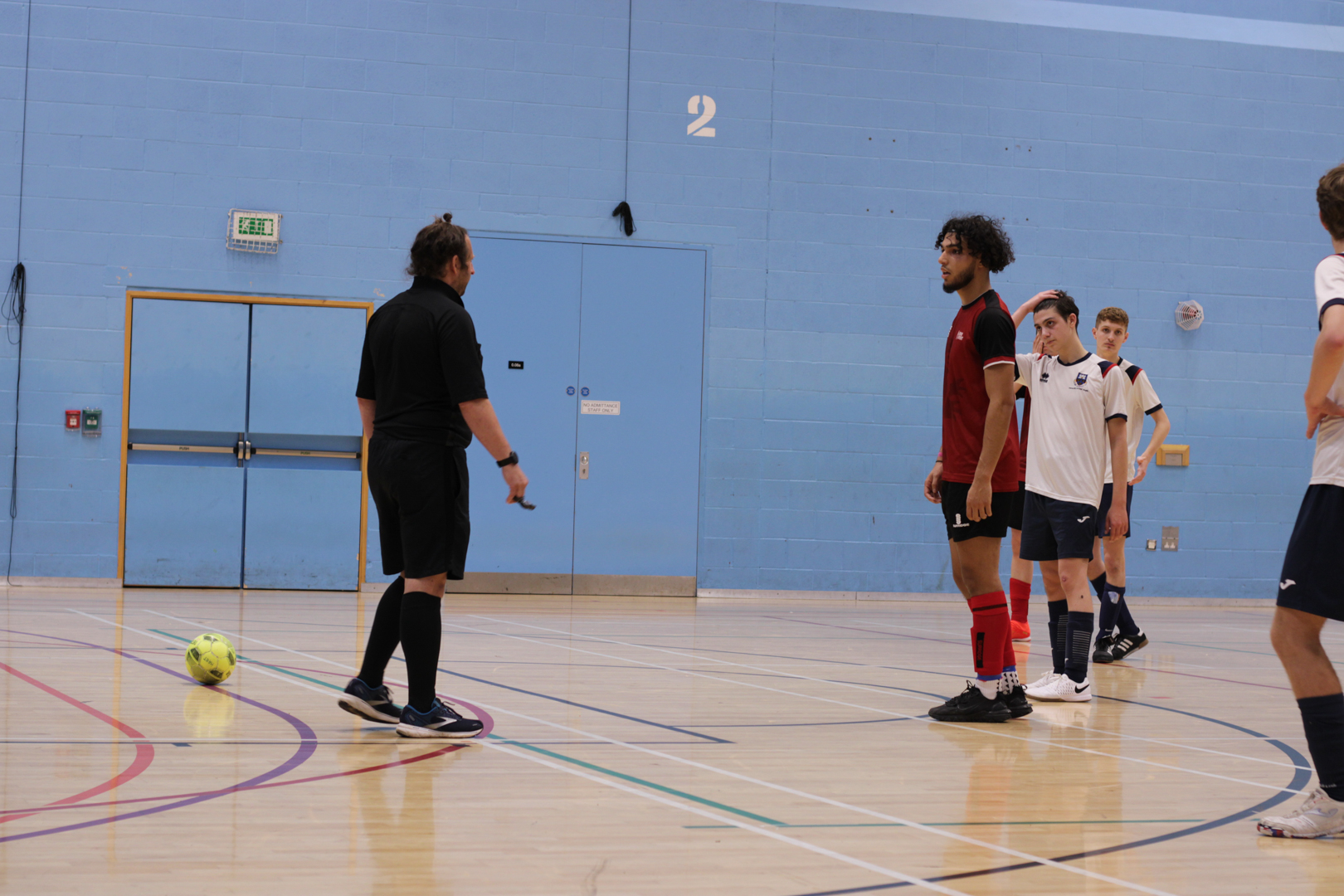 Referee and players preparing for a penalty during a futsal match.