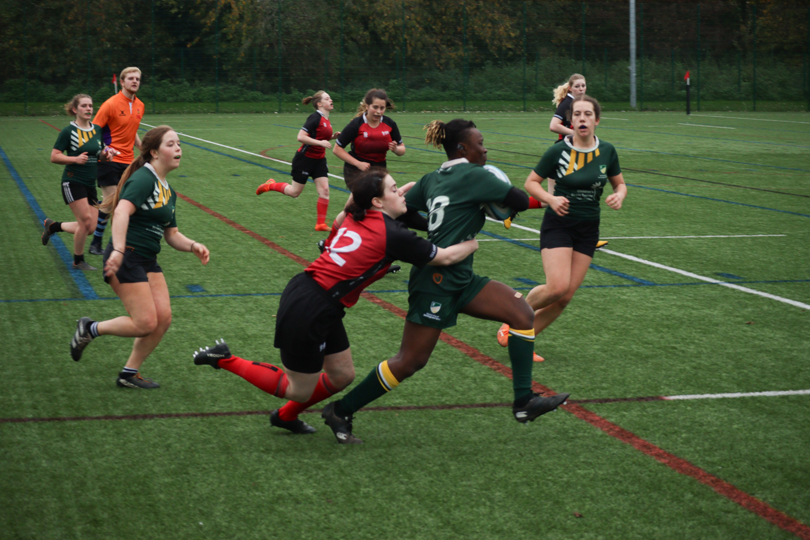 Rugby players in action on a field, with one player in red tackling a player in green.