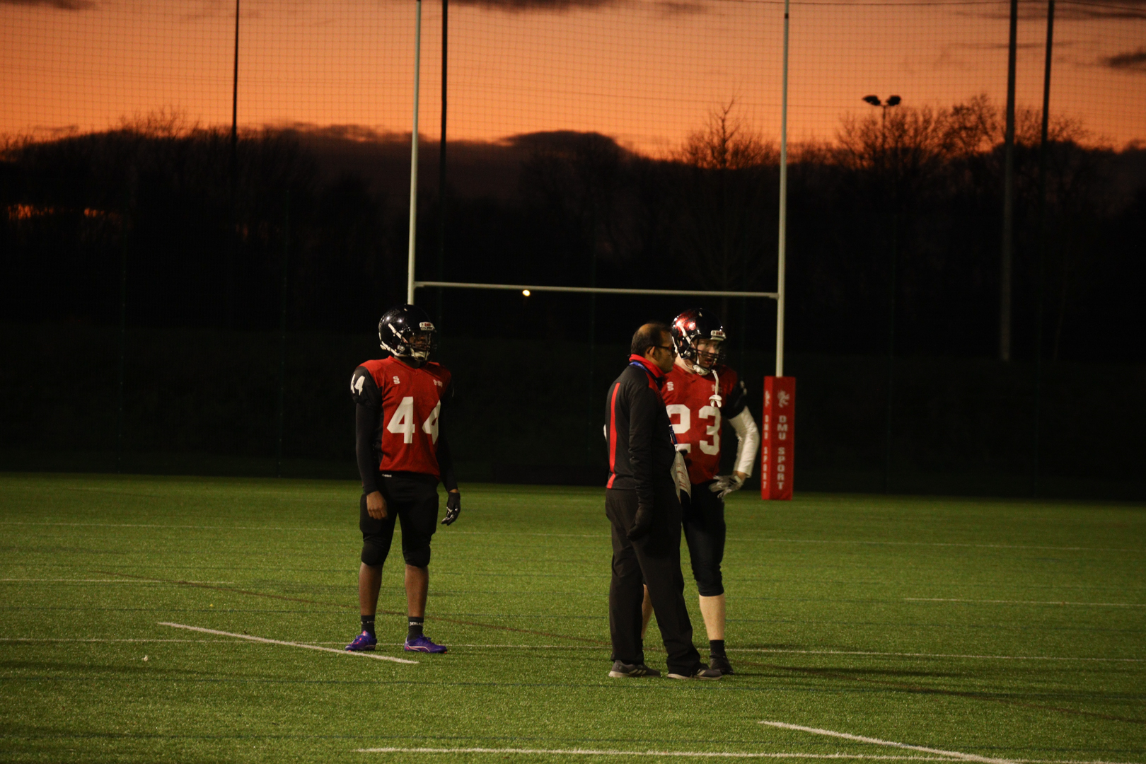 Two American football players and a coach on a court during a break in play.