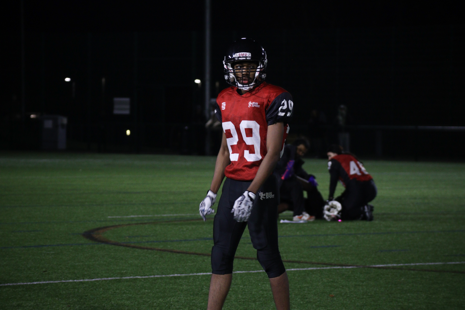 American football player wearing a red jersey with number 29 stands on a lit field at night.