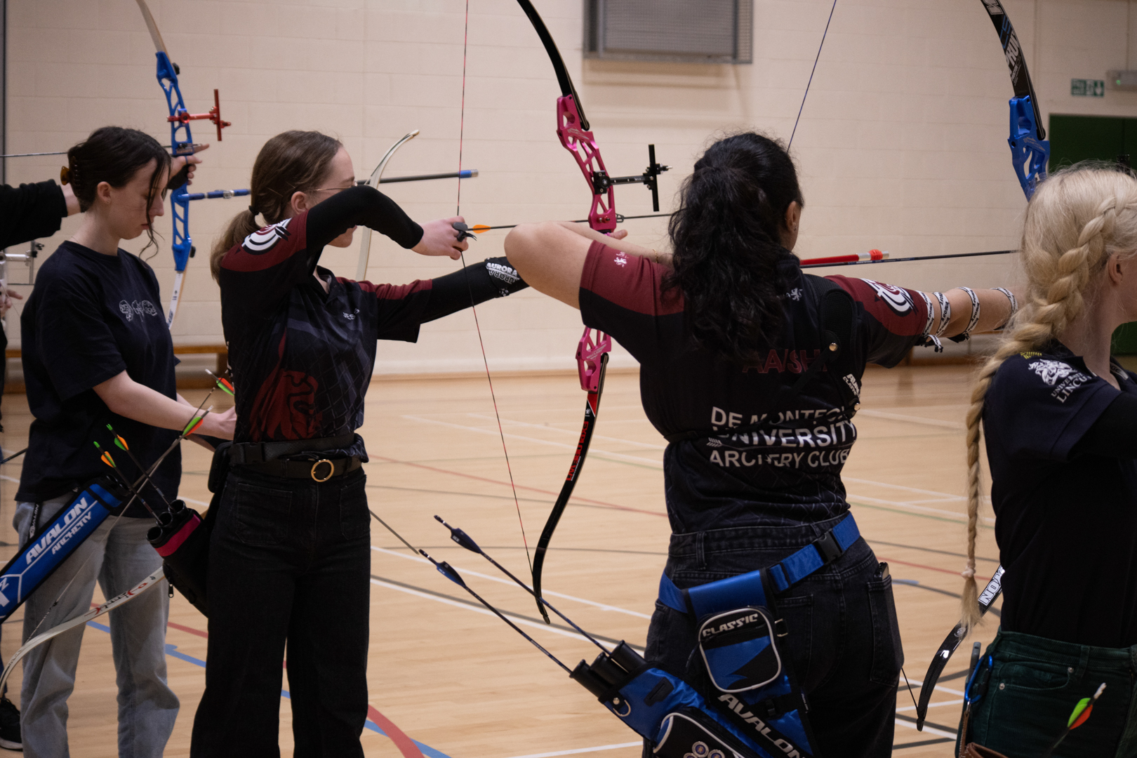 Person aiming a bow at archery targets in an indoor gymnasium.