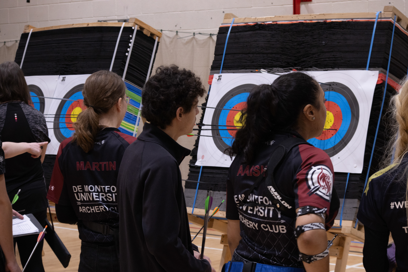 People examining targets with arrows in an indoor archery range.