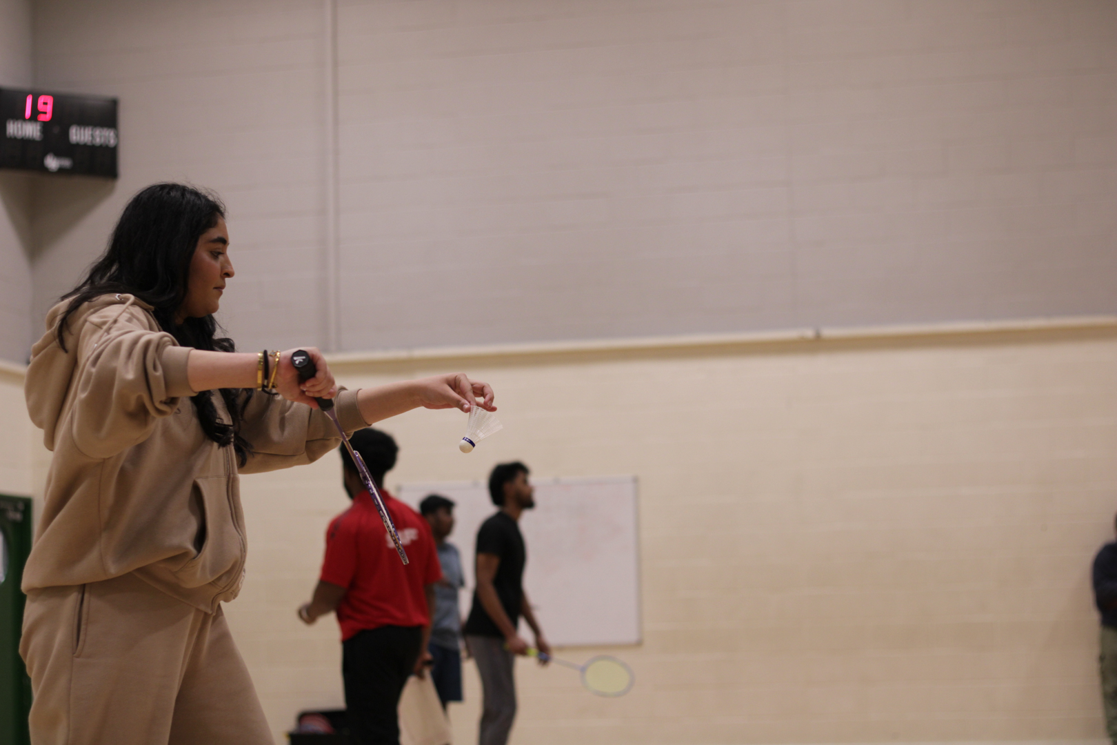 A person prepares to serve while others stand in a gymnasium. 