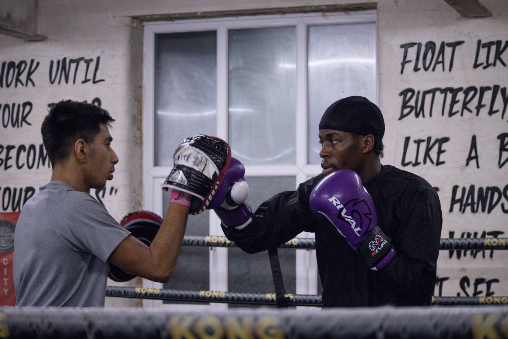 Two men practicing boxing in a gym, with motivational quotes on the wall.
