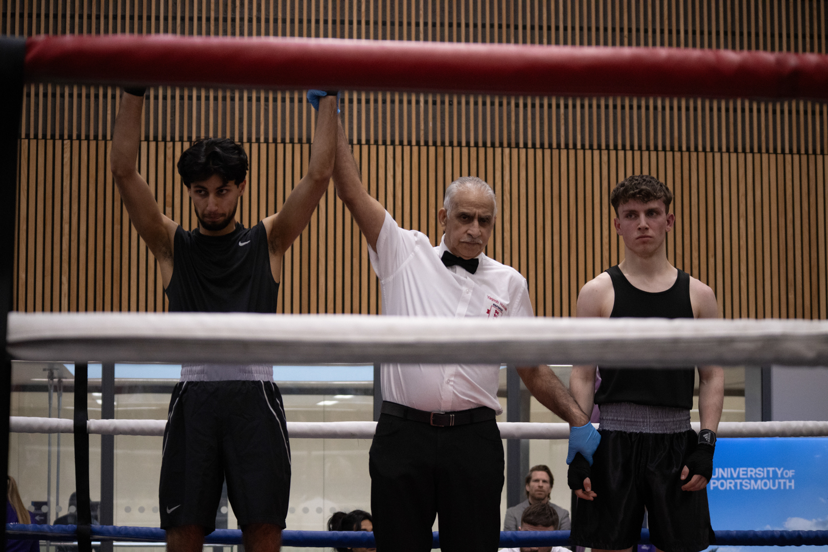 Boxing referee raises the arm of one boxer to declare victory, while the other boxer stands nearby.