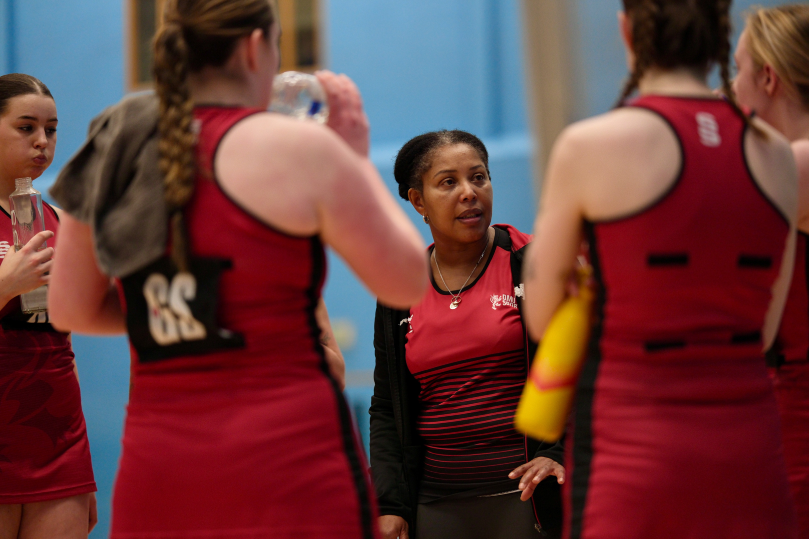 A coach talks to a group of netball players wearing red uniforms during a break in the game.