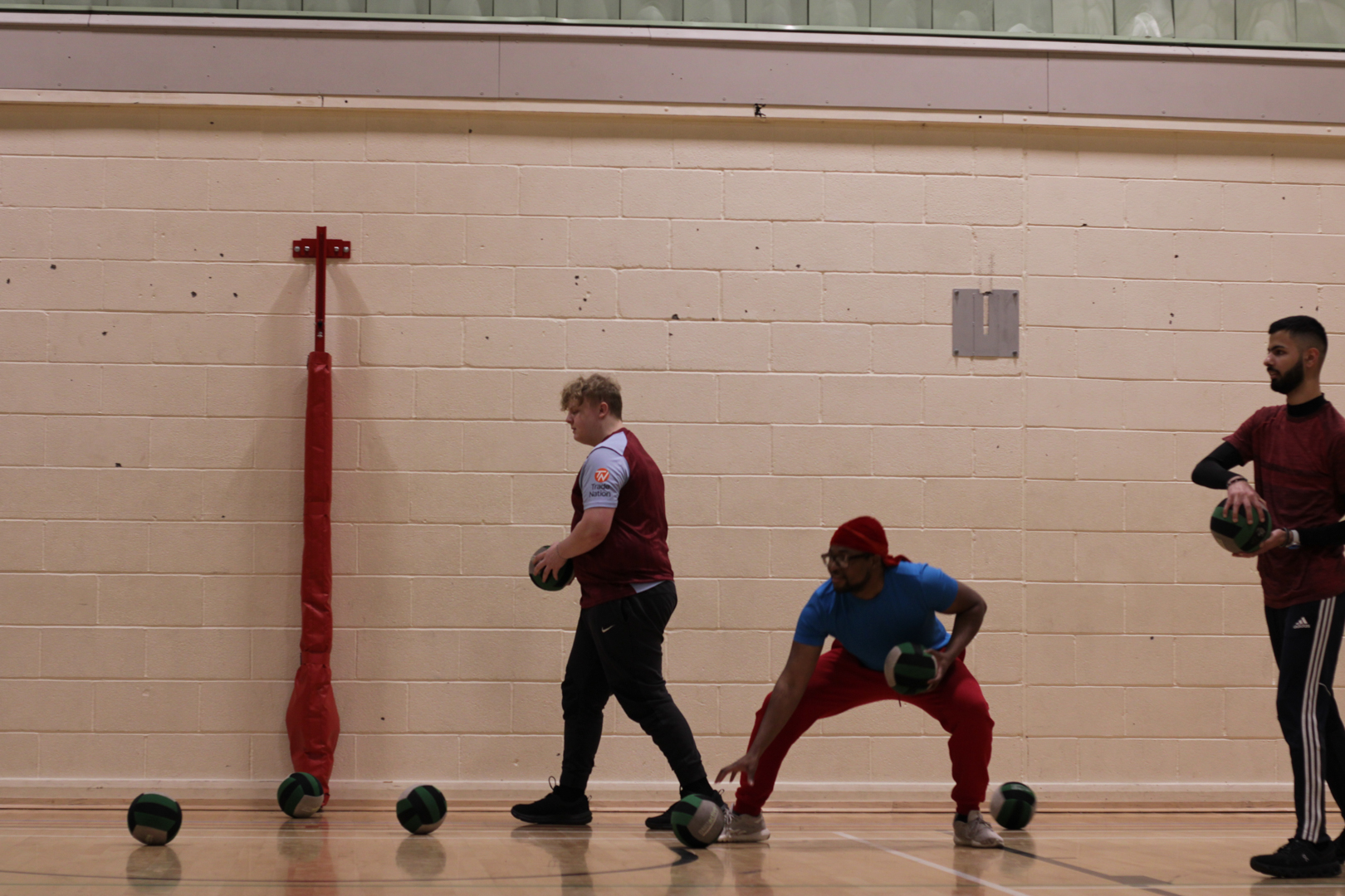 Three people playing dodgeball in a gym, each holding a ball and preparing to throw.