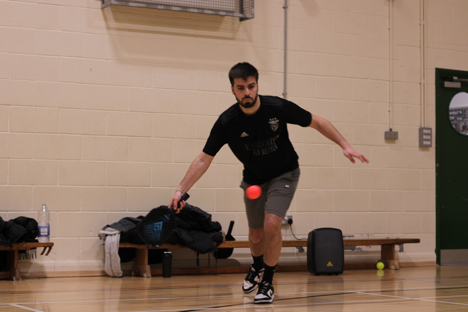 Person playing indoor pickleball, preparing to hit a ball with a paddle in a gymnasium.
