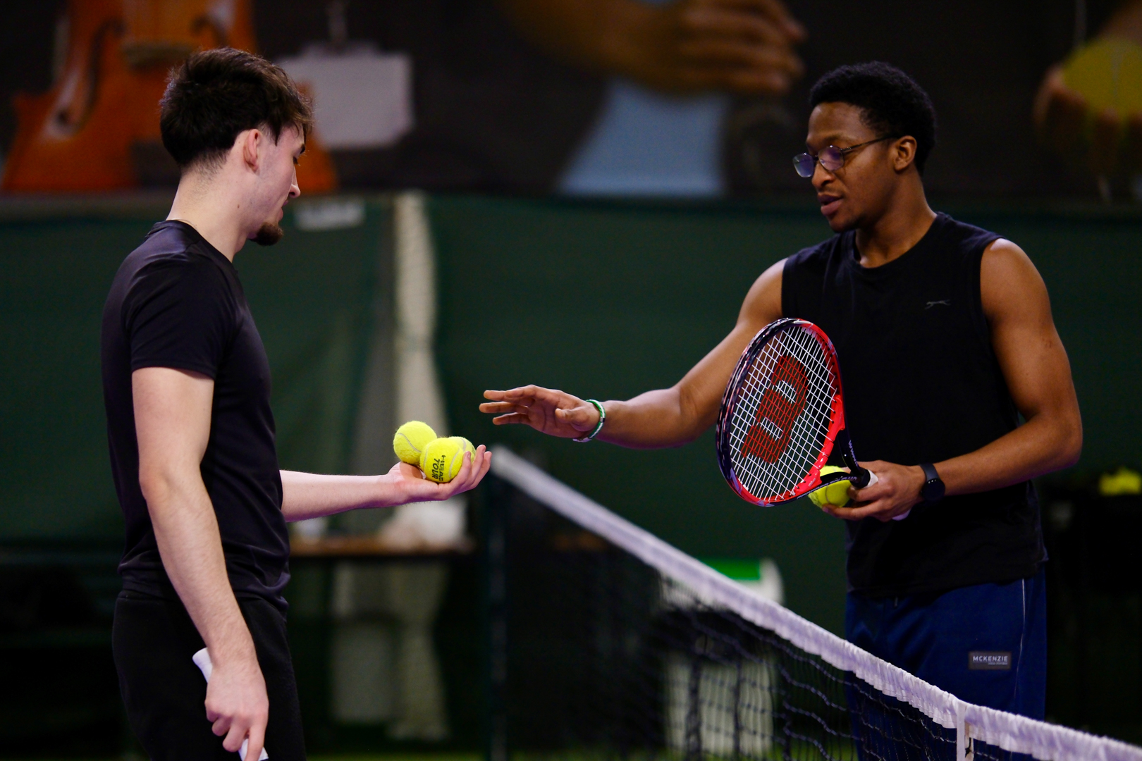 Two tennis players exchanging tennis balls over a tennis net.