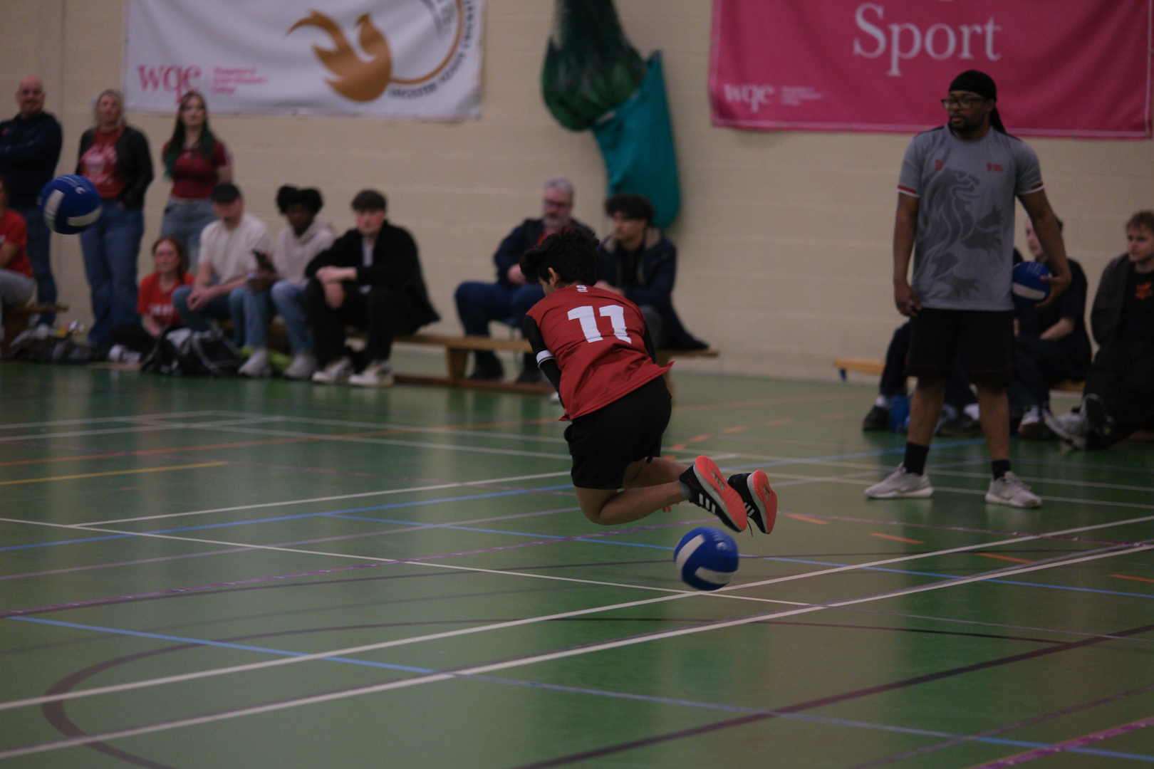 A Student in a red shirt dodges a ball while spectators watch in the background.