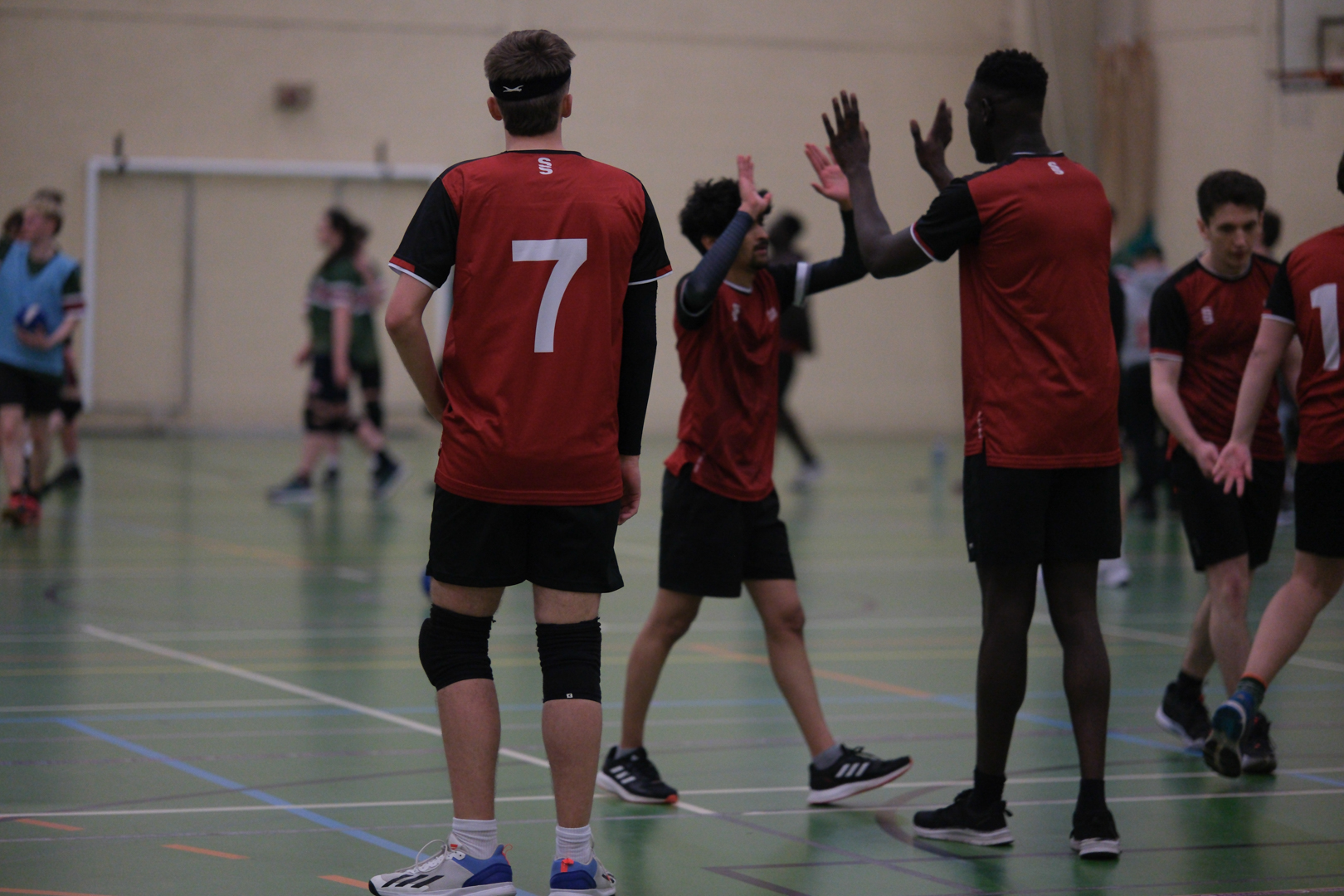 Dodgeball players in red shirts high-five on an indoor court during a game.