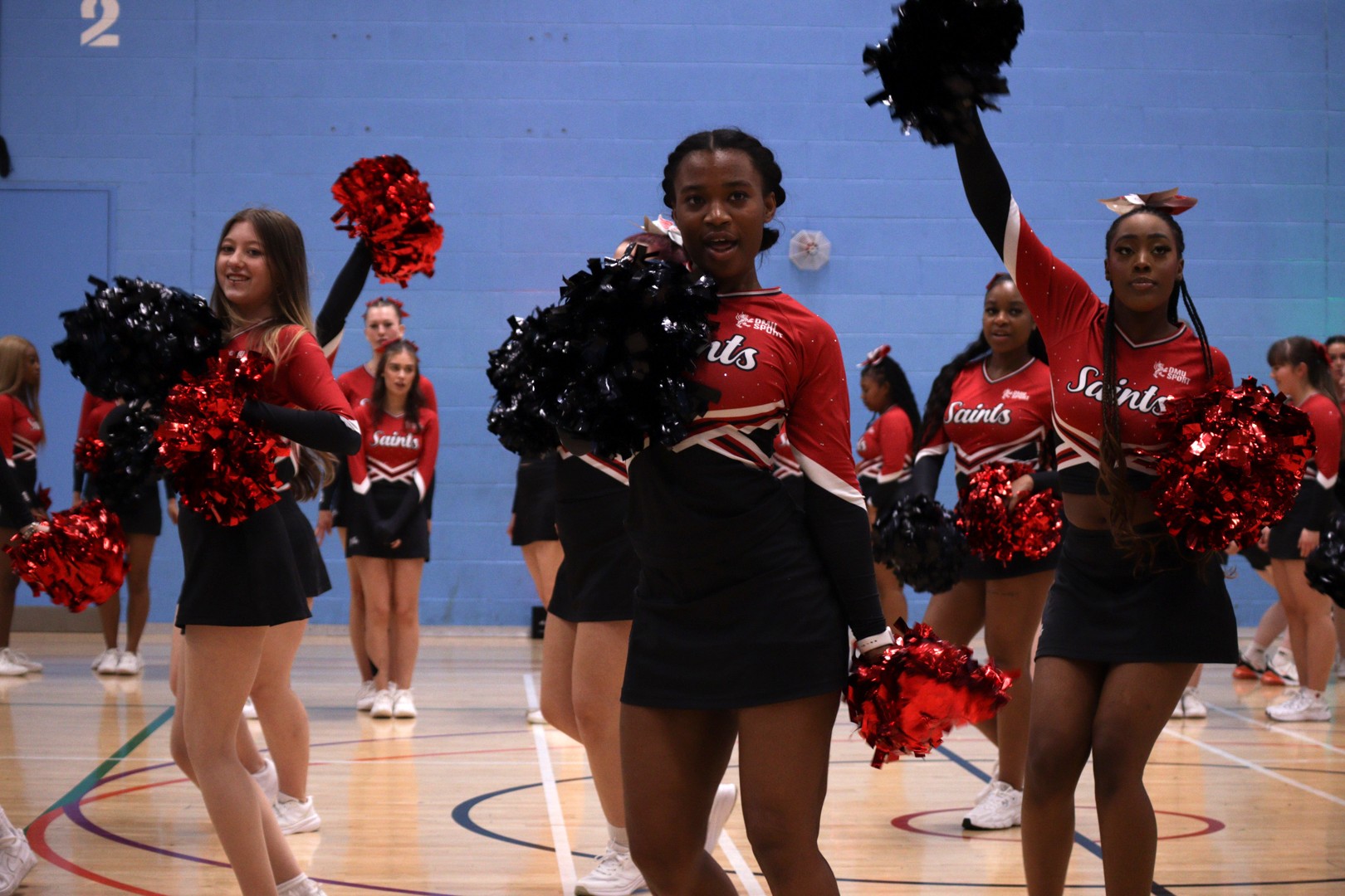 Cheerleaders in red and black uniforms performing a routine indoors with pom-poms raised.