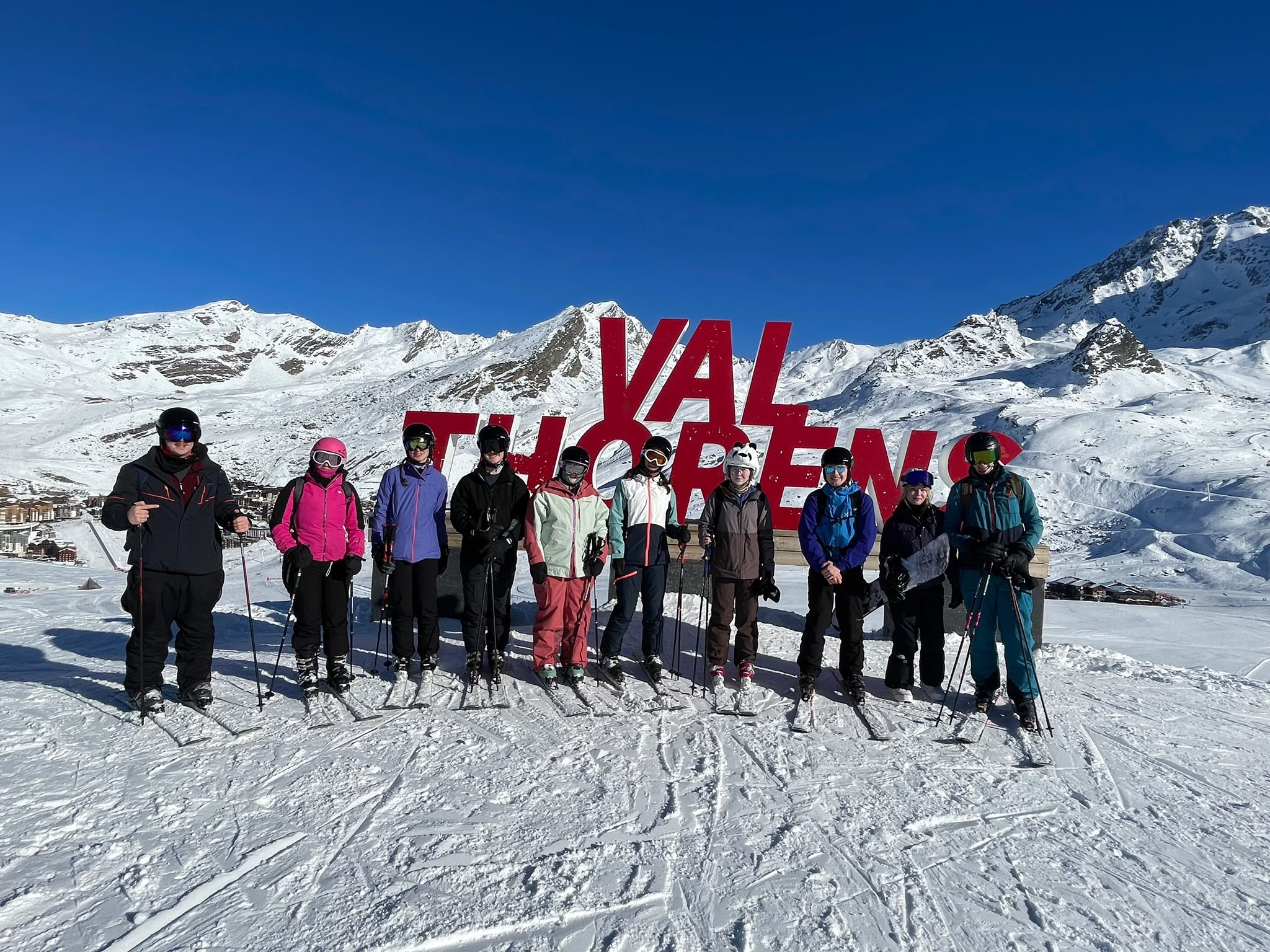 A group of people stand in front of large red "Val Thorens" letters on a snowy mountain slope.