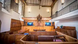 Empty courtroom with wooden benches, judge's bench, two computer monitors, and a coat of arms on the wall.