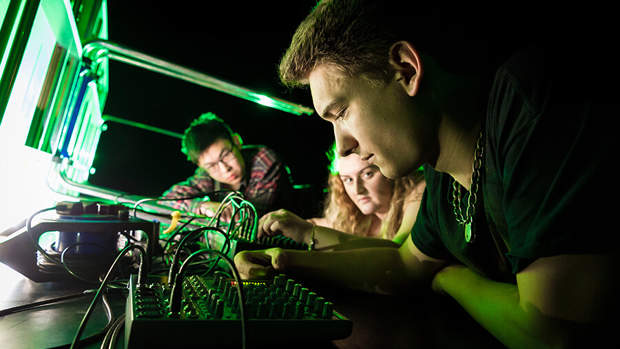 Two people closely examining electronic equipment under green lighting.