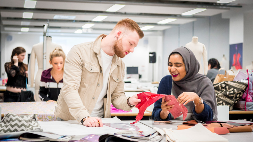 Two students examining fabric in an open classroom in the Vijay Patel building