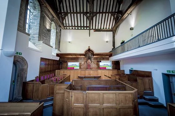 Interior of a historic courtroom with wooden benches, a judge's bench, and a high ceiling with exposed beams.