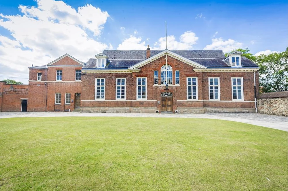 Brick fronted hall in front of a large grassy lawn.