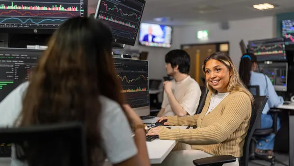 Students working at computers displaying financial charts in the trading room
