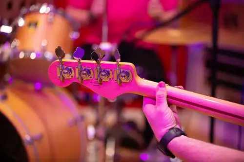 Close-up of a person playing a bass guitar with a drum set visible in the background.