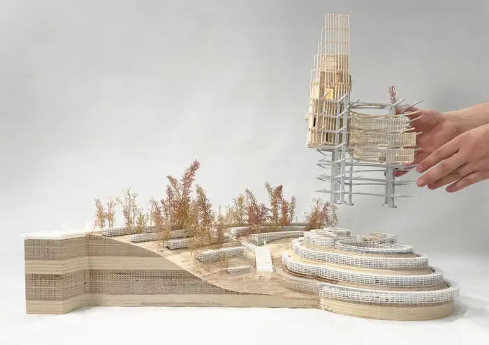 Architectural model with layered terrain, abstract wooden structures, and a hand adjusting a wireframe building element. By Raven Schneider.