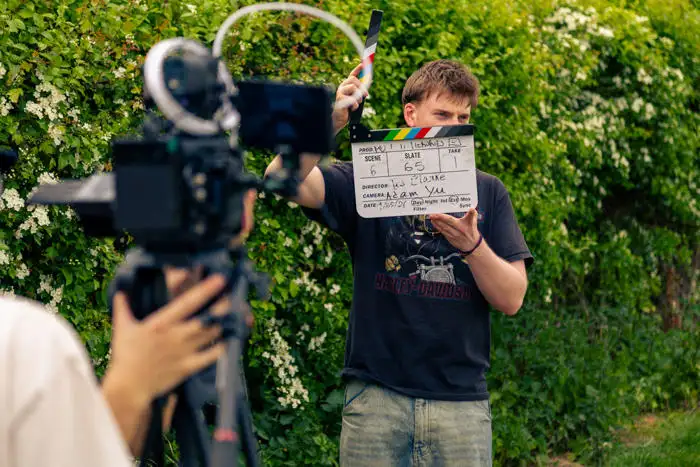 Person holding a film clapperboard in front of a camera outdoors, preparing to record a video scene.