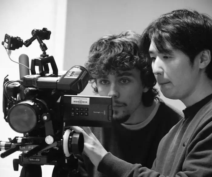 Two people operating a professional video camera, focusing intently on the equipment.