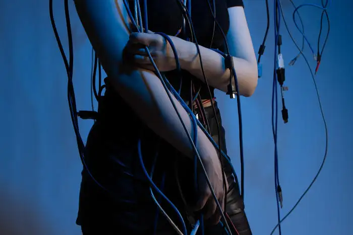 Lily Cohead: A photo of a woman's midsection on a blue background; various cables are wrapped around her arms.