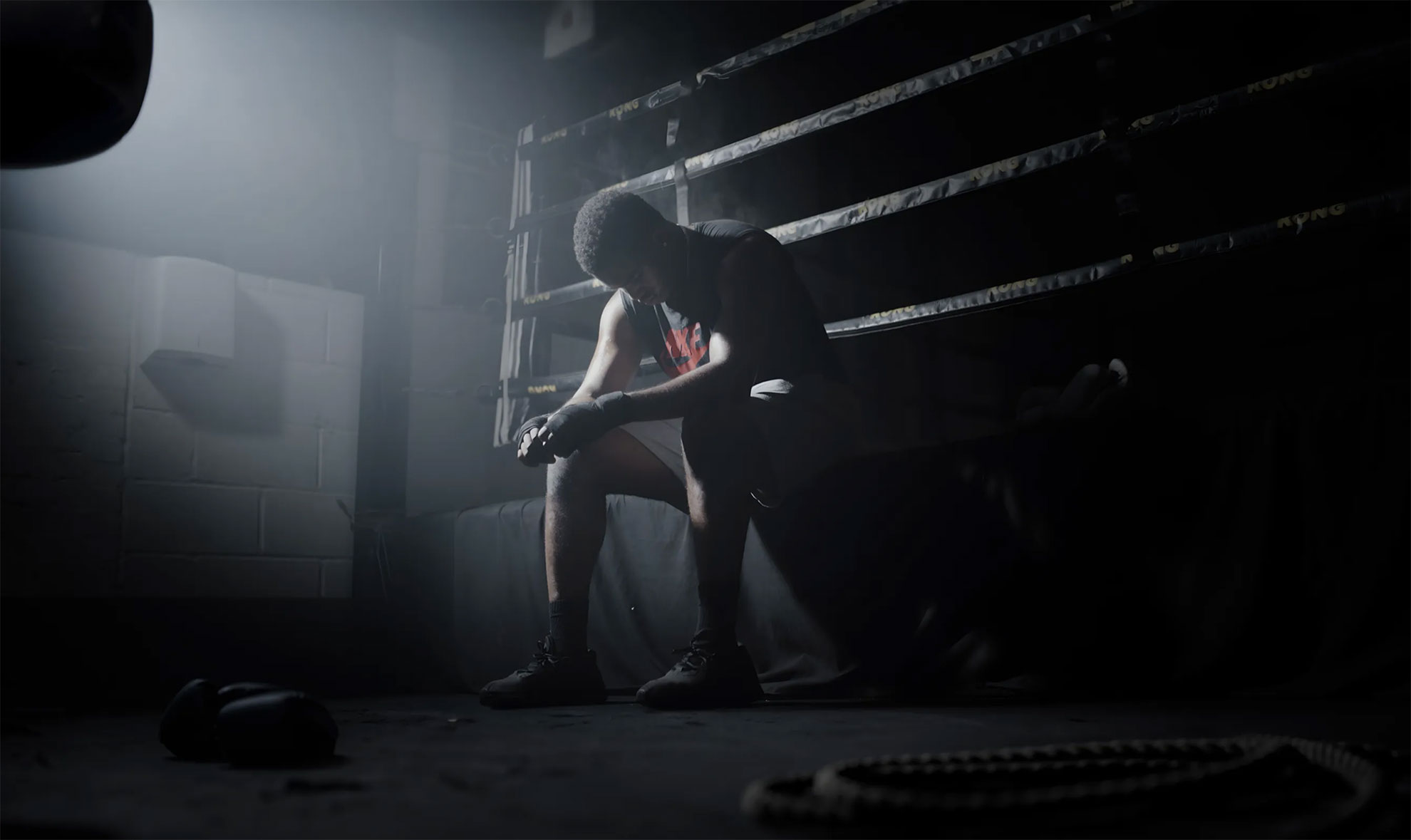 A spotlit man sitting at the edge of a boxing ring looking down at the floor.