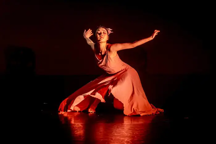 Dancer in a flowing red dress performing a dramatic pose on stage under warm lighting.