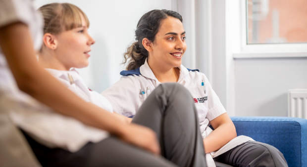 Two people in medical uniforms sitting and smiling in a bright, indoor setting.