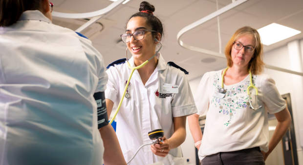 Two healthcare professionals in uniforms walk through a hospital corridor, appearing focused and engaged.