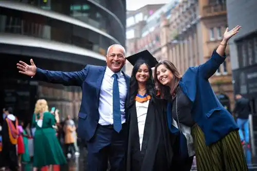 Three people smiling and celebrating outdoors, with one wearing a graduation cap and gown.