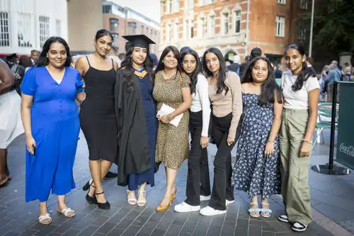 Eight women stand together outside on a city street, smiling and posing for a group photo.