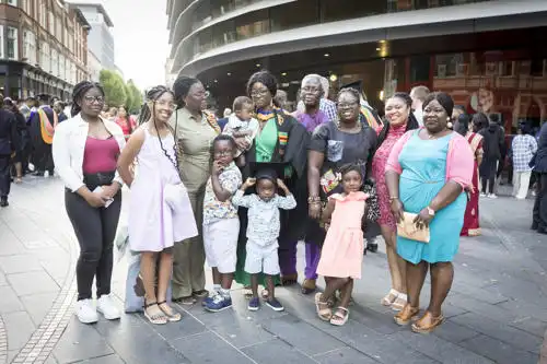 A group of adults and children pose together outdoors on a city street, dressed in colorful and formal attire.