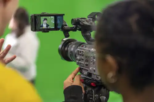 Student working with a professional camera in front of a green screen studio