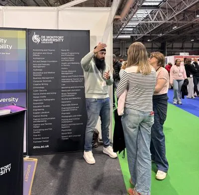 Dal speaking with two students at the DMU exhibition stand, discussing university opportunities.