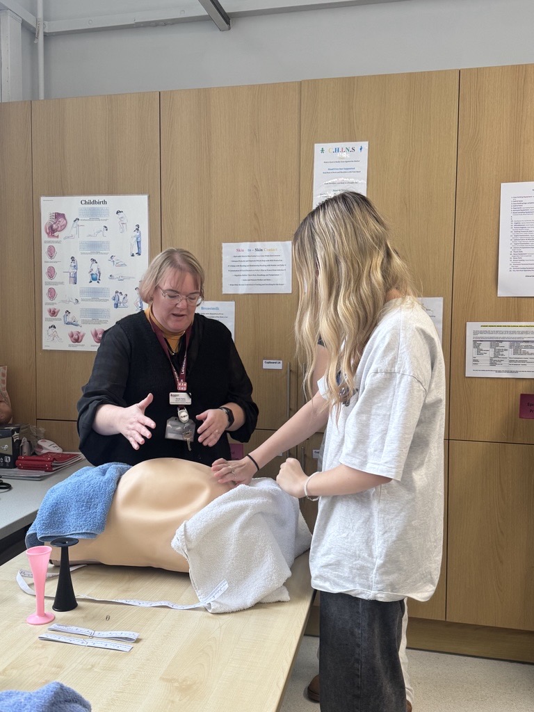 A student using a midwifery teaching simulator during a taster session, with an academic guiding them. 