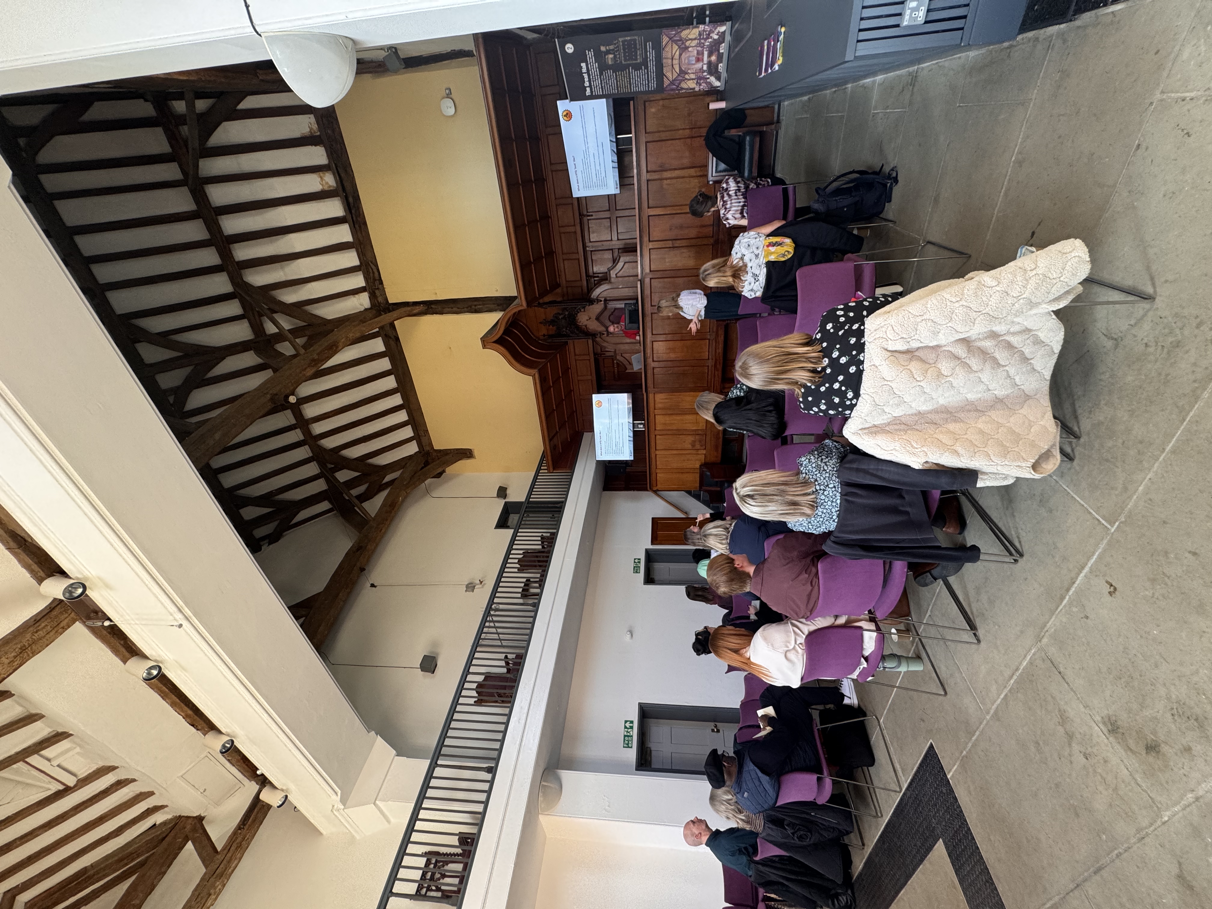 Teachers seated at DMU, watching presentation slides on large screens during a professional development event.